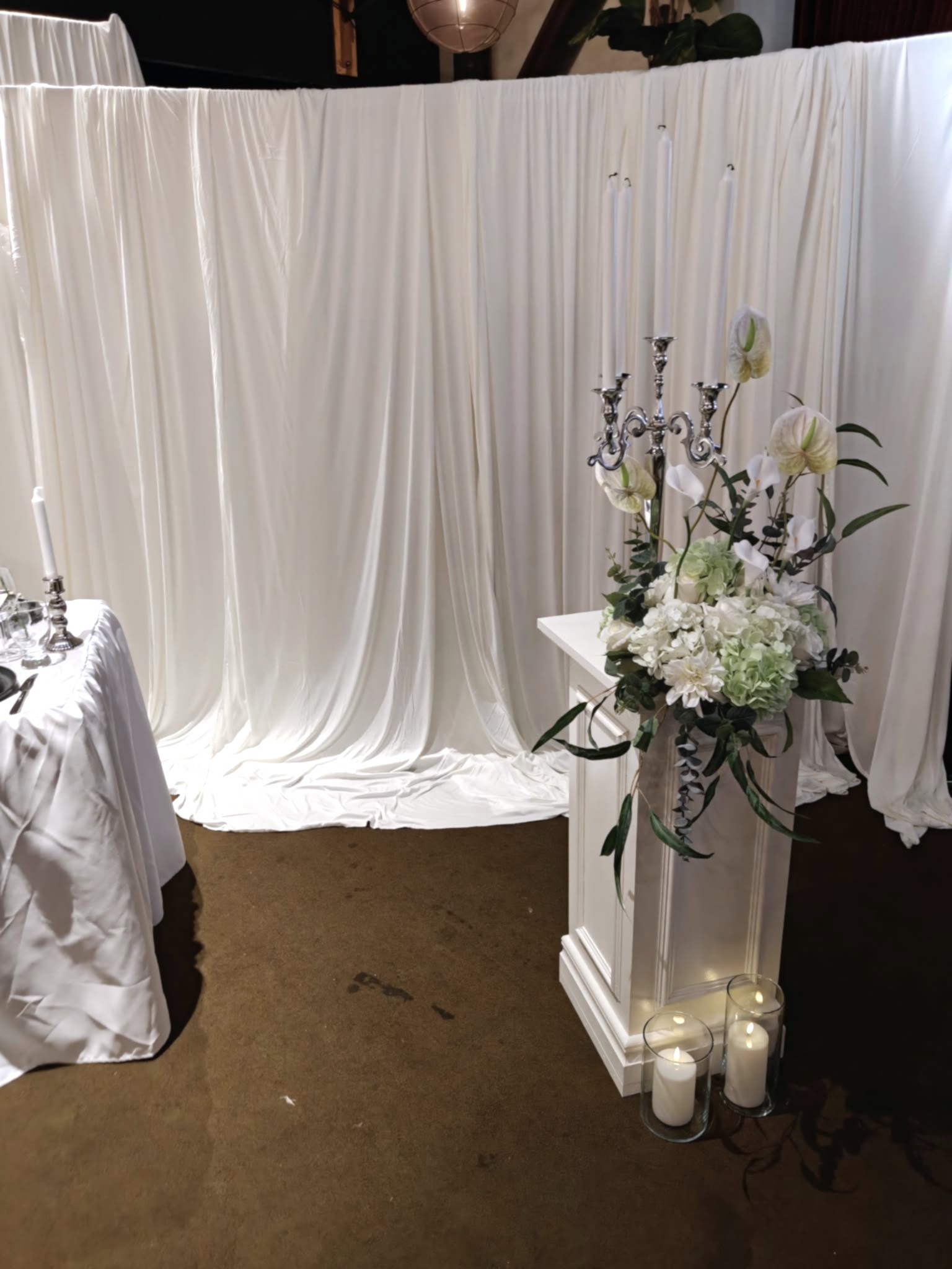 Vit lyxig pedistal med silver kandelaber, eleganta blommor och vit elegant bakgrund